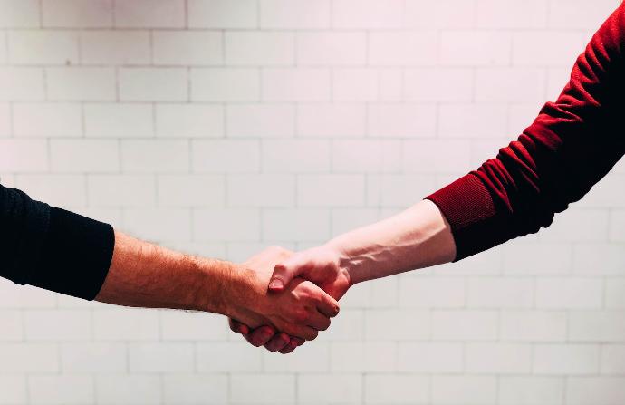 two person shaking hands near white painted wall